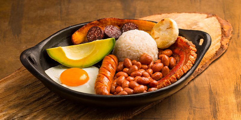 Comer bandeja paisa, una manera de conocer la cultura colombiana – Bandeja paisa servida en mesa de madera | Marca País Colombia